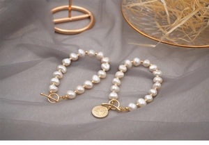Detail of baroque pearl bracelets with T-bar clasp and gold coin pendant on tulle