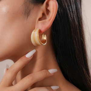 Close-up of a model wearing a beige resin C-shaped hoop earring with a golden post