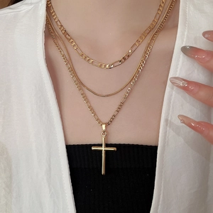 Close-up of three-layered 18k gold plated Figaro and snake chain necklace with cross pendant