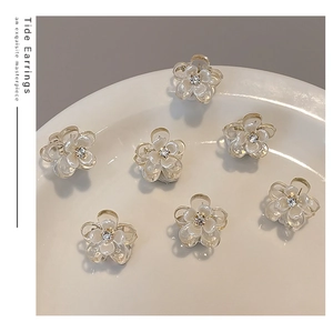 Close-up of seven mini cream camellia hair claws with rhinestones on a ceramic plate