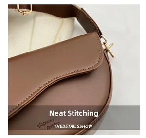 Detail view of the fine stitching and pale gold metal buckle on a brown leather saddle bag