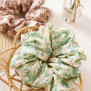 Detail of floral oversized hair scrunchies in green and pink fabric inside a woven basket