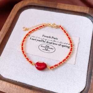 Detail eines roten geflochtenen Armbands mit 18k Goldperlen und rotem Bohnenanhänger