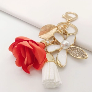 Floral keychain with red fabric rose, white enamel flower and white tassel on white background