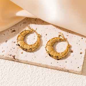 Detail of gold hollow bamboo earrings on stone base with satin background texture