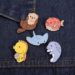 Detail of five ocean creature enamel pins including sea otter and pufferfish on denim