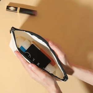 Detail showing hands opening the canvas makeup bag to reveal its interior capacity
