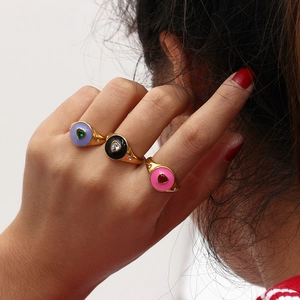 Détail de trois bagues dorées en émail violet noir rose avec des pierres en forme de cœur