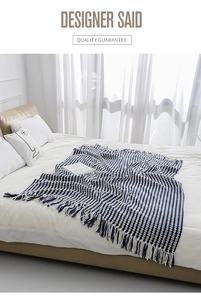 Detail of blue and white geometric knitted blanket with decorative tassels on a bed