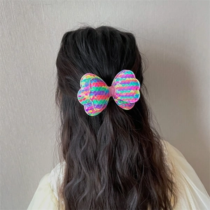 Girl wearing a colorful sequined bow hair clip on long wavy hair, cute vibrant hair accessory