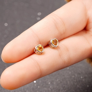 Macro view of small heart-shaped stud earring featuring a bright yellow gemstone setting