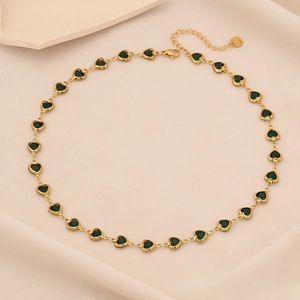 Elegant gold necklace featuring green heart-shaped gemstones on beige fabric background