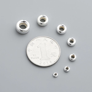 Various sizes of S925 sterling silver spacer beads arranged around a coin for scale