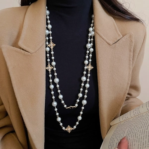 Detail view of a double-layer vintage pearl necklace with golden cross charms on a model