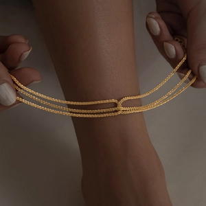 Detailed view of the layered triple golden chain worn on the ankle with high-shine finish
