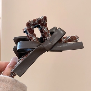 Close-up of brown leather bow and plaid fabric texture on a stylish shark hair claw