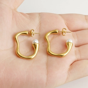 Boucles d'oreilles créoles dorées irrégulières avec perle blanche dans la main
