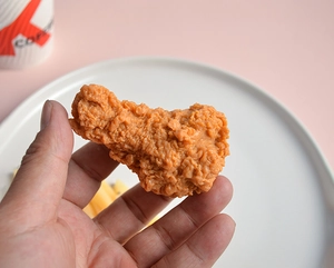 Close-up of realistic PVC fried chicken drumstick model held in hand with crispy texture