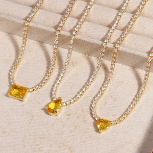 Macro detail of three gold tennis necklaces with square, teardrop, and heart yellow crystals