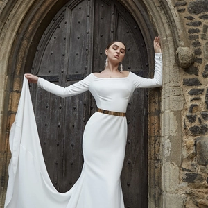 Elegant white off-shoulder bridal gown with long sleeves and wide gold metallic belt