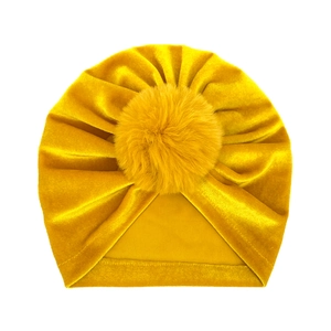 Detail of mustard yellow velvet baby beanie with a large fluffy pompom on top