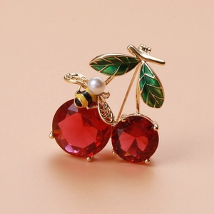 Macro detail of cherry and bee brooch with red zircon and pearl on peach background