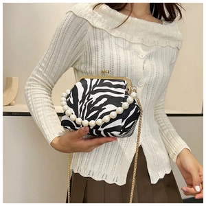 Cow print shoulder bag with elegant pearl handle and gold chain strap held by model