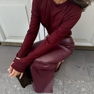Dettaglio della gonna midi in ecopelle bordeaux opaca a vita alta con spacco laterale e maglia