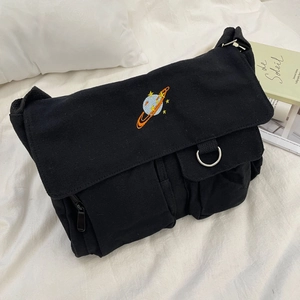 Close-up of black canvas messenger bag featuring colorful planet embroidery and pocket detail