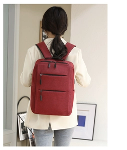 Back view of a burgundy business backpack with multiple zippers worn by a model in a room