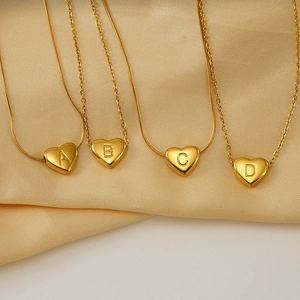 Gros plan de pendentifs cœur dorés avec lettres A, B, C et D sur tissu en satin doux