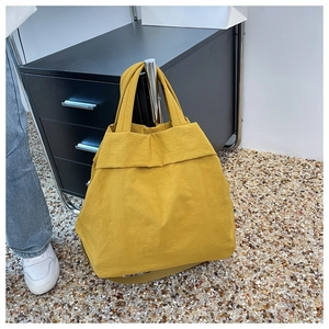 Detailed view of a yellow nylon tote bag with shoulder straps hung for size reference