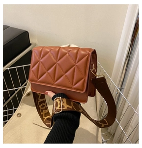Detail view of brown quilted crossbody bag featuring a stylish patterned wide shoulder strap