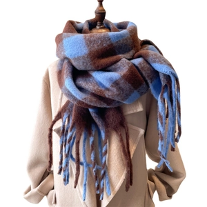 Blue and brown plaid winter scarf with fringe tassels on a beige coat model