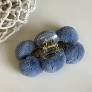 Detail view of a blue plush ball hair claw clip with transparent base on white background