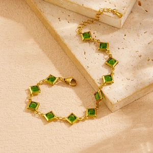 Detail view of gold chain bracelet with green faceted square gemstones on stone plate