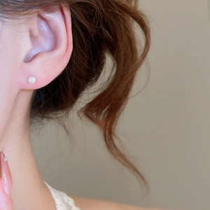 Close-up of minimalist white pearl stud earring worn by a model in a natural setting