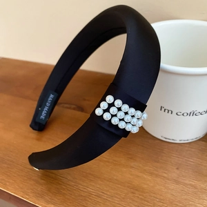 Detailed view of black satin headband with elegant pearl accents and handmade woven label