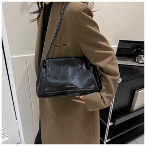 Close-up of black pleated PU leather shoulder bag with gold chain strap on a model