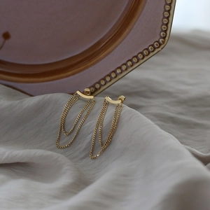 Detailed view of gold tassel earrings with curved smile bar design on fabric