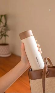 Detail of leak-proof matte insulated water bottle being placed in a stylish bucket bag