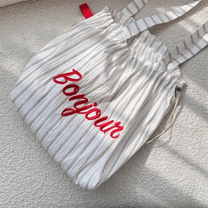 Detail of red Bonjour embroidery on a beige striped canvas drawstring tote bag