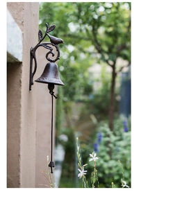 Close-up of vintage cast iron doorbell with bird ornament and rope in garden setting