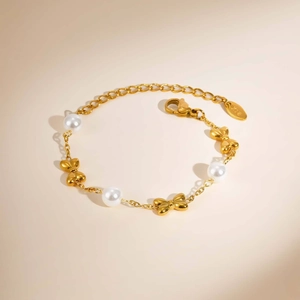Golden girl's stainless steel bracelet with white pearls and bow charms on beige background