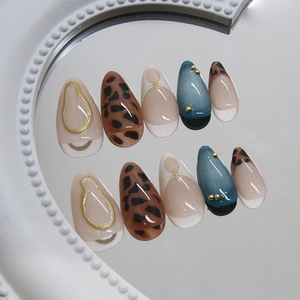 Leopard print press-on nails with blue cat eye finish and gold 3D accents on white tray