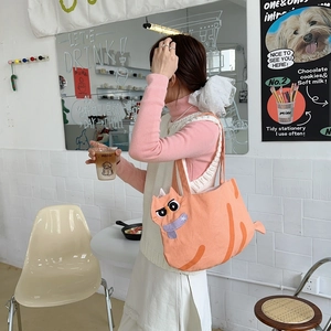 Vibrant orange cartoon cat canvas tote bag with 3D ears shown in a minimalist cafe