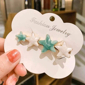 Starfish hair clip with blue and white enamel on gold metal, held in hand on card
