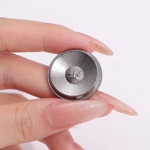 Minimalist silver metal button badge with radial texture and scale emblem held by hand