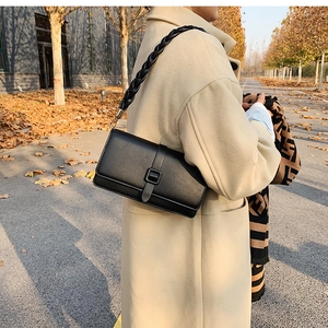 Detail of black crossbody bag with wide woven strap and leather buckle in autumn setting