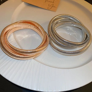 Close-up of gold and silver multi-layer metal elastic snake bone bracelets on a ceramic plate
